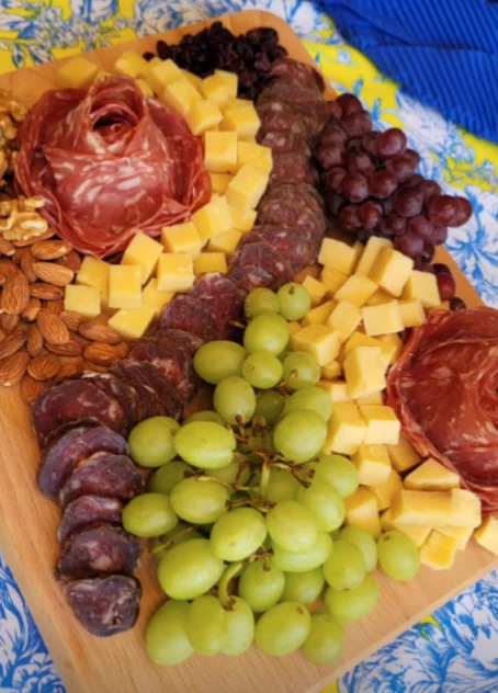 A visually stunning cheeseboard arranged with elegance, including rustic grapes on the vine, color-coordinated fruits, and separate soft cheese presentation.